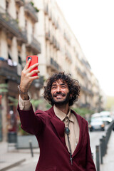 Handsome young man taking a self portrait while walking through the city. Urban millenial with beard and earring using a smart phone and smiling carefree outdoors. Lifestyle concept..