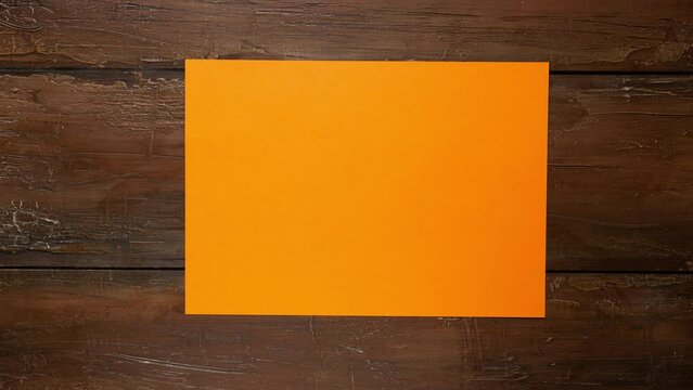 Orange color empty paper wrinkles making a paper ball and a blank sheet on textured brown wooden background with copy space. Stop Motion video available for both vertical and horizontal use.