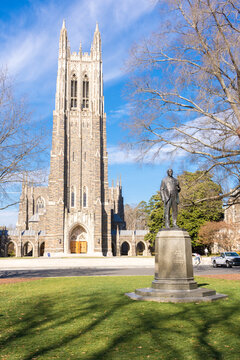 Exterior of Duke University Chapel, Durham, North Carolina, with statue of James Duke on green lawn, bright sunshine, and blue sky and clouds.