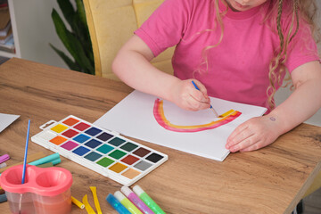 activities with a child concept, a cute girl with blond long hair draws a rainbow on paper