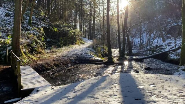 Tranquil forest scene of a small river flowing under a small wooden bridge with snow on the ground 