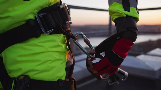 Industrial climber hooks a metal carabiner with a jumar to a loop on a safety belt close-up