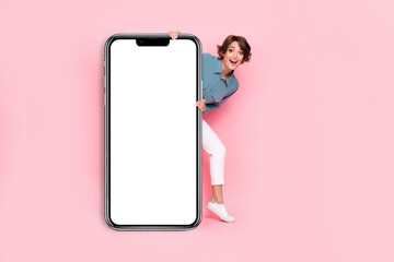 Fototapeta na wymiar Photo of cheerful lady hide look big modern device telephone present demonstrate show empty space isolated on pink color background