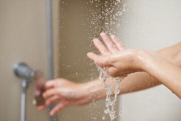 A woman uses hand to measure the water temperature from a water heater before taking a shower - obrazy, fototapety, plakaty