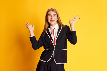 Success. Portrait of beautiful young girl, student in uniform posing with positivity over yellow studio background. Concept of youth, beauty, fashion, lifestyle, emotions, facial expression. Ad