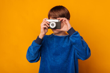 Teen boy looks through a vintage camera and trying the photographer profession.