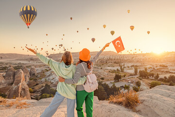 Girl friends travellers with turkish flag, hugging on a viewpoint and admiring view of flying hot...