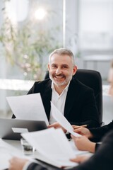 Smiling middle aged business man sitting in the office. A male businessman looks over documents and smiles during a business meeting in a conference room.