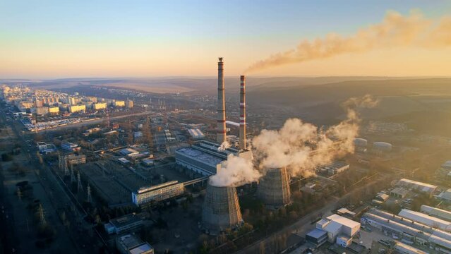 Aerial drone view of thermal power plant in Chisinau at sunrise, Moldova. View of pipes with felling steam, infrastructure around, cityscape on the background