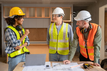 Architect colleagues mixed race working as a team discussing data working and tablet, laptop with on on architectural project at construction site at desk.