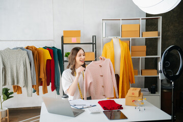 Beautiful lady blogger showing clothes in front of the camera to recording vlog video live streaming at her shop. Online Shopping Cart notion..