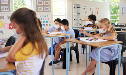 Learning, covid teaching and studying young students sitting in a school classroom indoors. Education of youth, children and kids with masks looking and working on class work in a pandemic