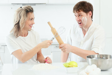 Husband and wife quarrel in kitchen while cooking. Comic and cheerful confrontation between man and woman in kitchen. Background..