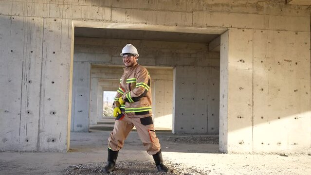 a cheerful positive male builder in a white hard hat and uniform is dancing on the background of construction slow mo