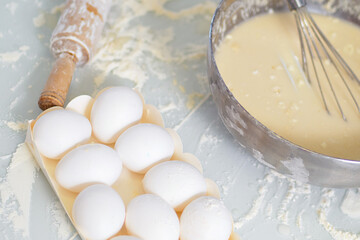 Chicken eggs are on kitchen table. Flour and cup with liquid dough. Preparation of festive dessert or pie. View from top. Background..