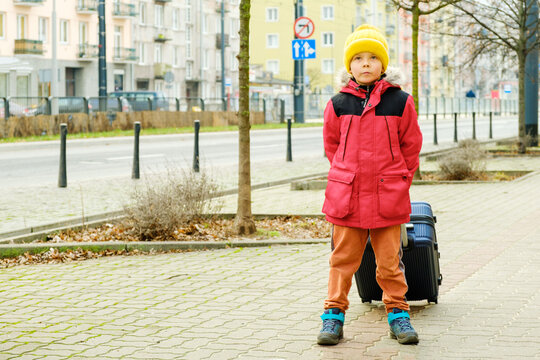 Six-year-old boy with suitcase near road in city..