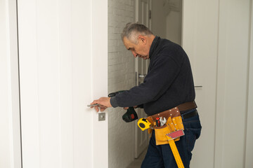 Mature man himself installs the door hinges with a screwdriver