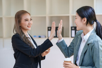 Two happy Asian businesswoman giving high five together in the office