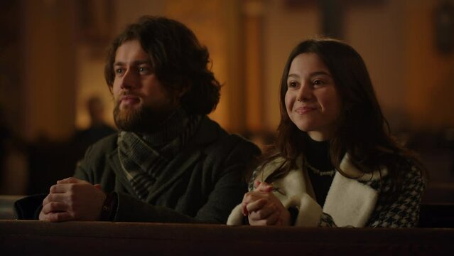 Close-up of a married couple sitting in a catholic church. A man and a woman sit with their hands clasped and smiling during a Sunday service.