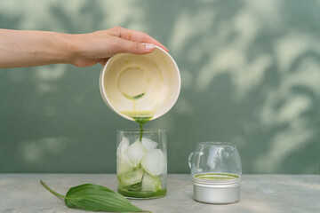 Close-up of a woman pouring whisked matcha green tea into a glass filled with ice cubes to make an iced matcha latte drink