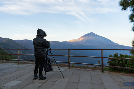 Turista joven capturando momento de fotografía en cámara mirrorless montada en trípode del majestuoso Teide, con chaqueta de invierno en el amanecer