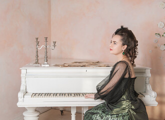 Beautiful thoughtful woman wearing green medieval vintage Victorian Style dress sitting near piano