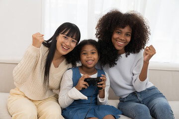 Young female and kid playing video game in home to relax together on weekend. Happy Asian women...