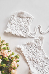 White knitted hat and flowers on white background. Stylish knitted clothes