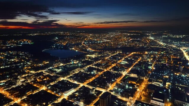 Aerial drone timelapse view of Chisinau at sunset, Moldova. View of the city with multiple residential buildings, park with lake, roads with moving cars, illumination