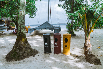 Three eco-friendly cylindrical recycling bins, colored in yellow, red, and blue for plastic, metal,...
