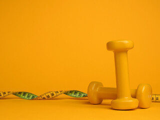 Yellow dumbbells with a tape measure on a yellow background