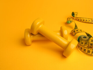 Fototapeta Yellow dumbbells with a tape measure on a yellow background obraz