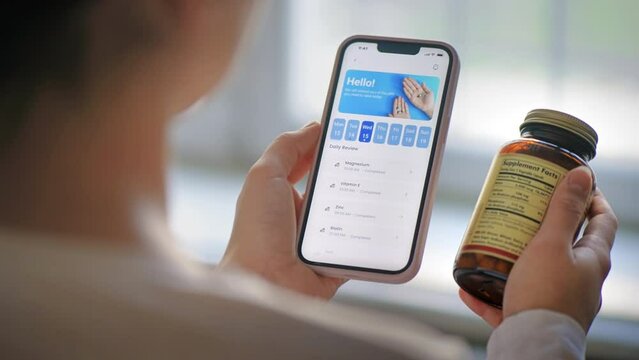 Close view of a person using smartphone with medication tracker app holding a jar of pills