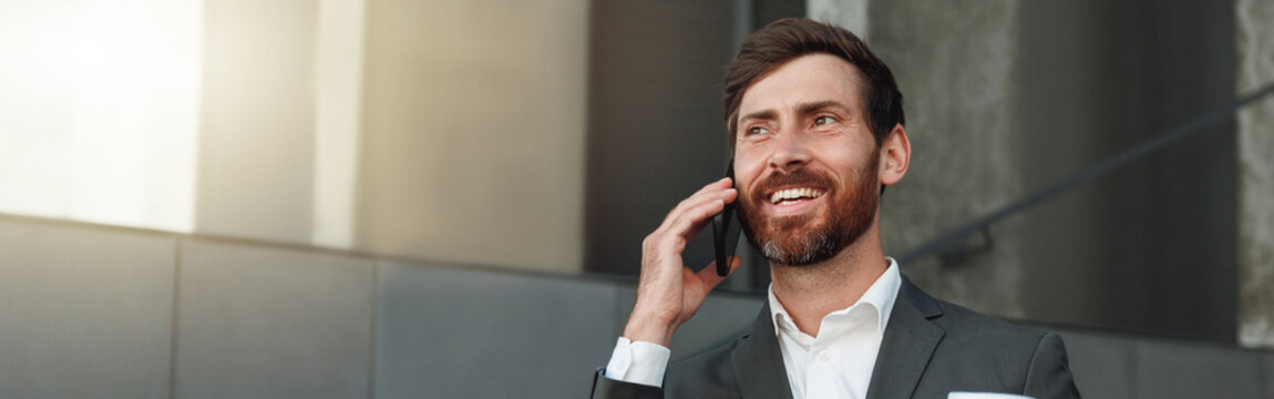 Smiling office worker in suit standing on stairs and drinking coffee during break near office
