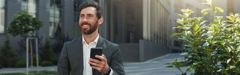 Attractive businessman holding phone sitting near office building during break