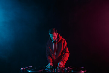 Club DJ mixing vinyl records with sound mixer on a party in night club. Young adult male person...