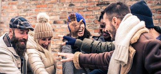 International friends giving five together wearing warm fashion clothes - Happy lifestyle concept with multicultural millennial people having fun together outside on winter holidays - Warm filter