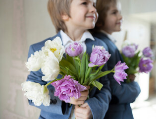 portrait elegant cute boy 6 years old. a young gentleman stands near a mirror, holds a bouquet of tulips in his hands, smiles. Happy smiling child with flowers. Mother's Day, Valentine's Day, Birthday