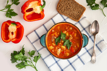 Hungarian goulash in a ceramic plate, bread, paprika, parsley on a white table