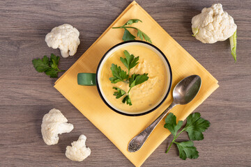 Creamy cauliflower soup in a green bowl on a wooden table, parsley leaves, cauliflower inflorescences