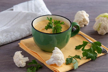 Creamy cauliflower soup in a green bowl on a wooden table, parsley leaves, cauliflower inflorescences