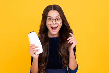 Teenager child girl showing bottle shampoo conditioners or shower gel isolated on yellow background. Hair cosmetic product. Mock up bottle. Excited teenager girl.