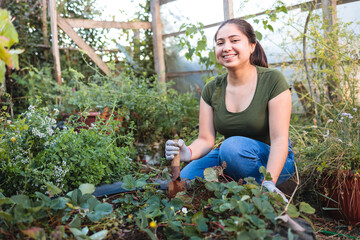 Young smiling latin farmer woman working with a garden spade shovel in her organic garden. 