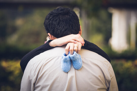 Mujer besa a su esposo mientras sujeta los zapatos de su futuro hijo