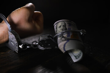 Hands of a fraudster with handcuffs on a background of us dollars. Fraud, cyber crime concept. Arrest of an entrepreneur in the workplace.