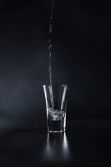 A Stream of Alcohol pours into a Glass against a black background. Water splash. Close up