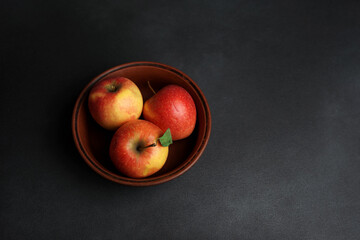 Fototapeta na wymiar Three Red juicy Apples Lie in a clay Plate against a black background. Copy space