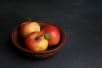 Three Red juicy Apples Lie in a clay Plate against a black background. Copy space