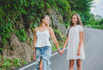 Cheerful, happy mother and daughter enjoying walk play outdoor. Funny family in white clothes barefoot on walkway. Green rocks at background.