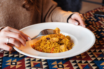 Unknown woman eating pilaf with meat at table in the restaurant
